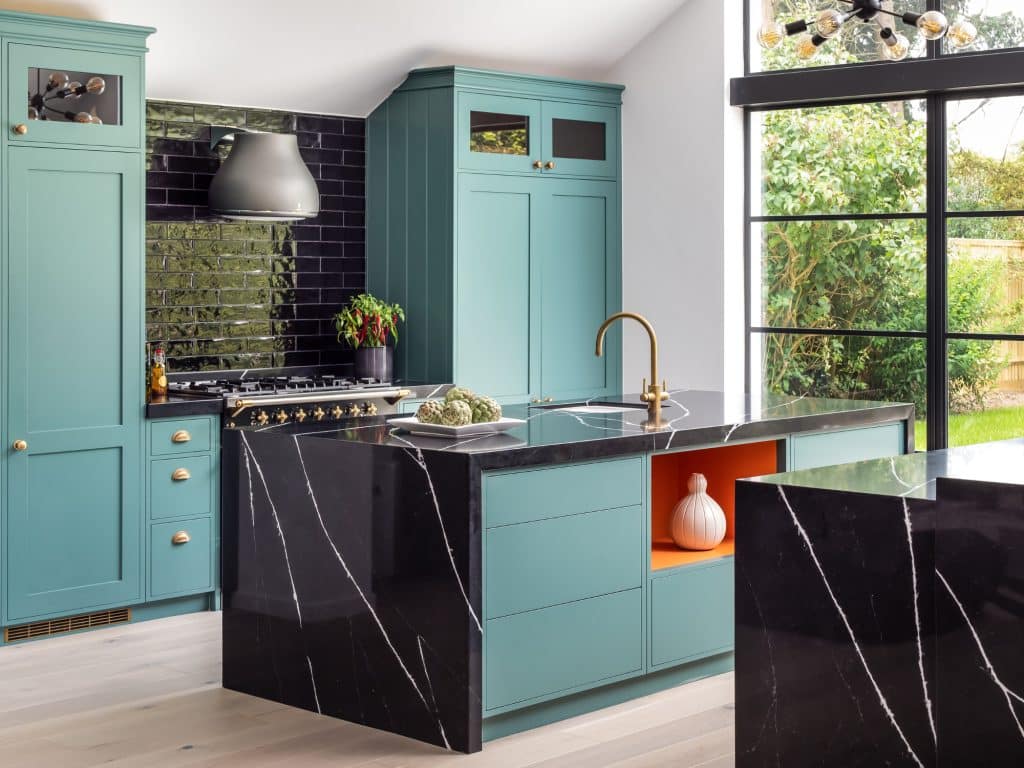 Black waterfall kitchen island with orange insert and handpainted green cabinetry.
