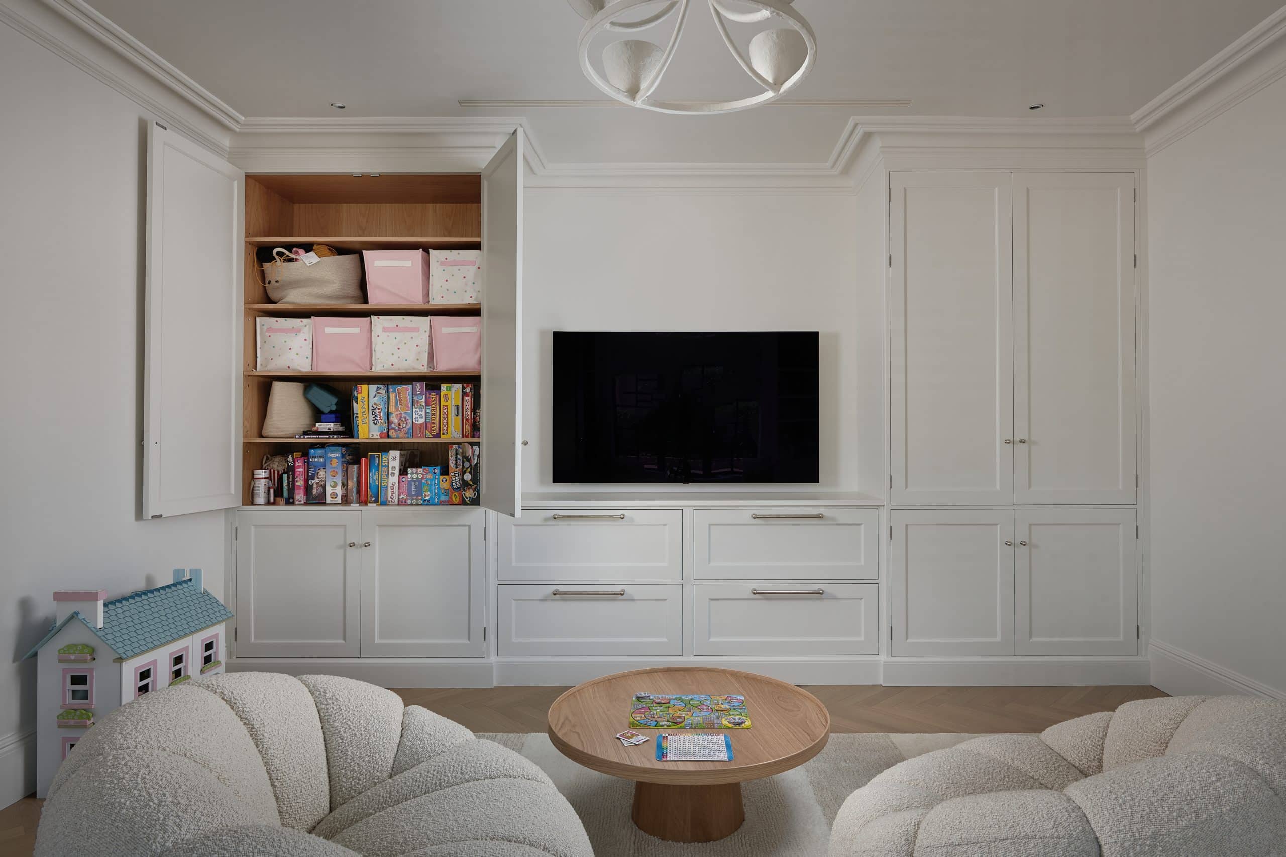 Children's luxury playroom with bookcases and bench seating, a media wall and cupboards for storage.